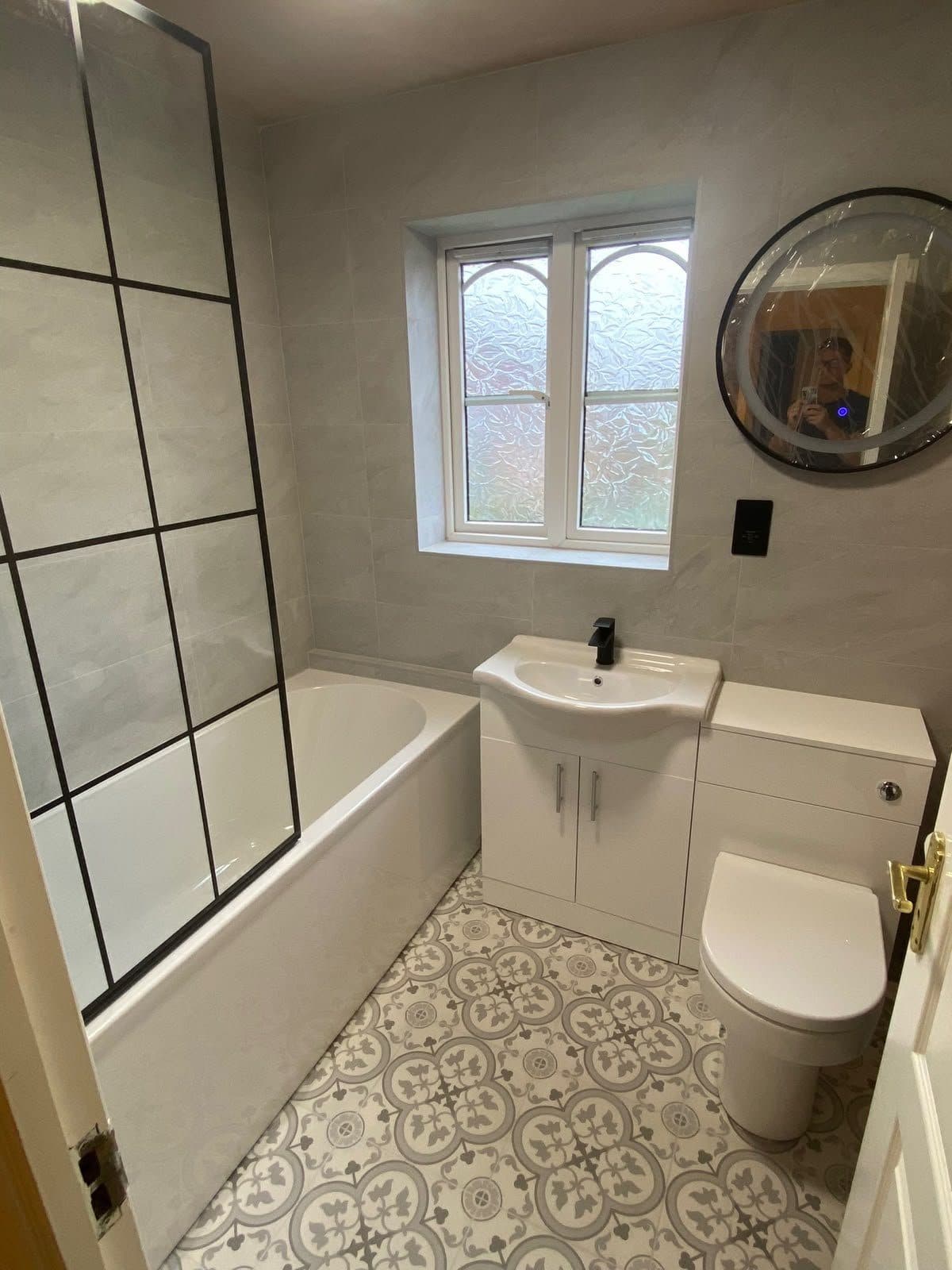 A bathroom with a bath, a black-framed shower screen and a patterned tiled floor