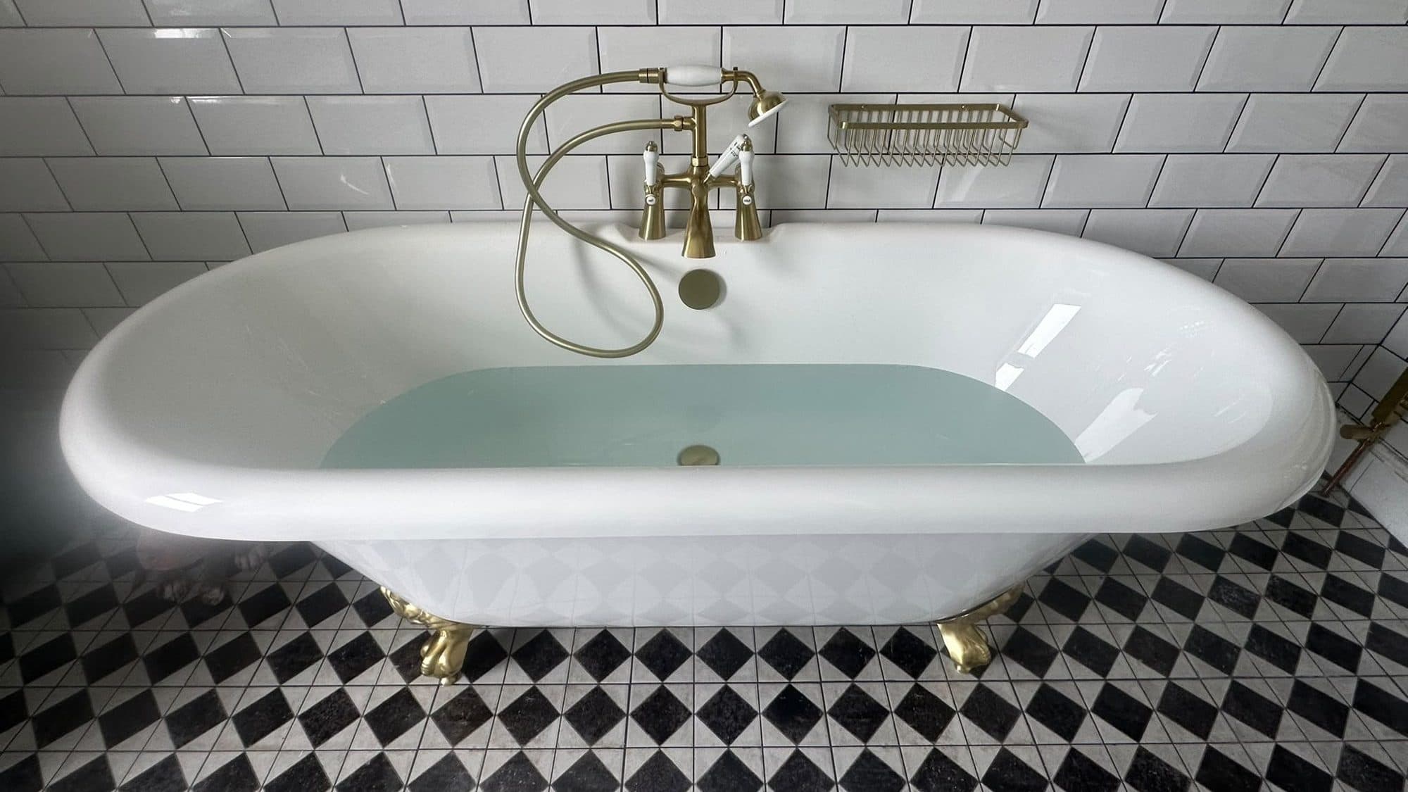 A roll-top bath with brass taps, white metro tiles and a black and white patterned floor