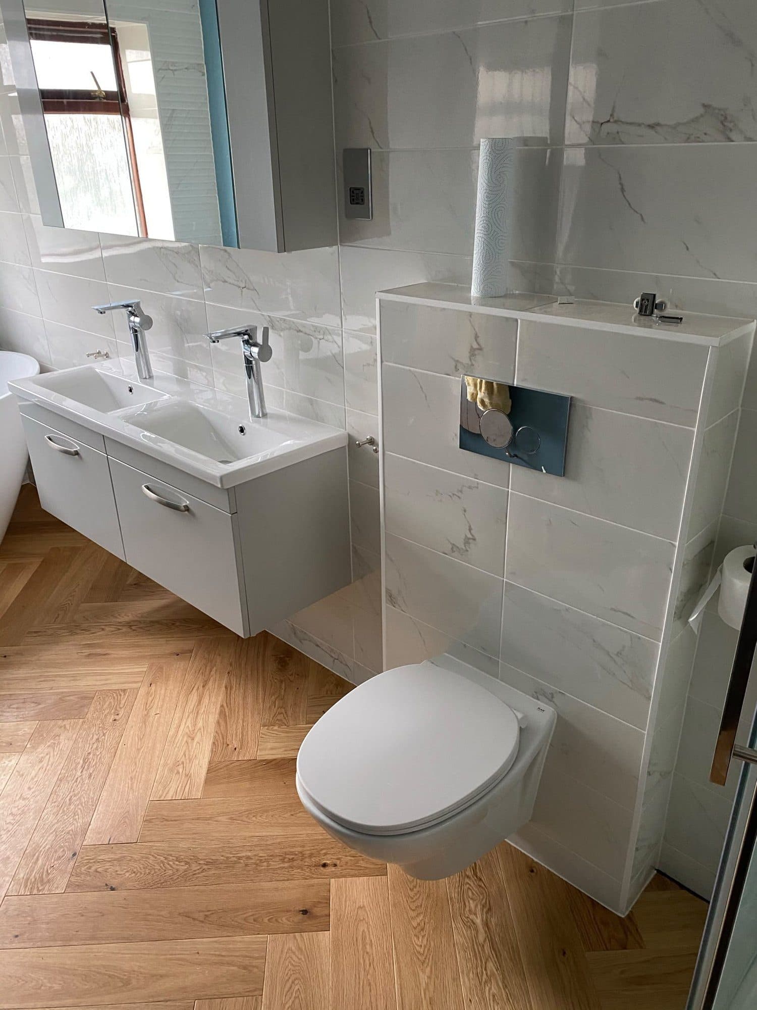 A bathroom with a wall-hung toilet, marble-effect wall tiles and a wood-effect floor