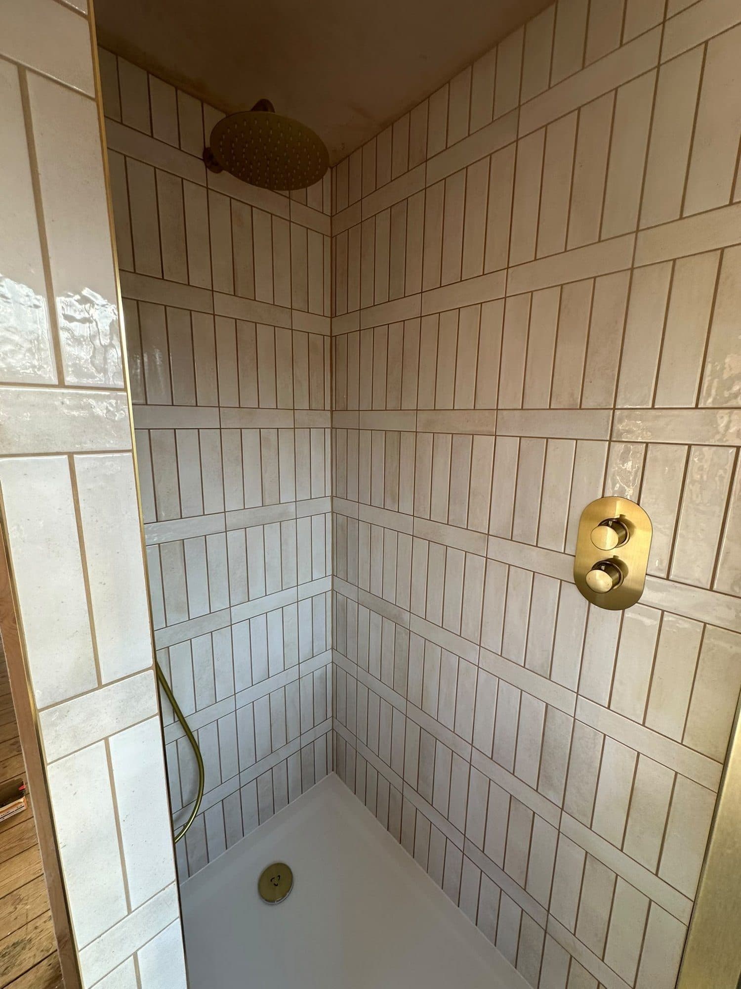 Vertical cream tiles in a shower with gold fittings